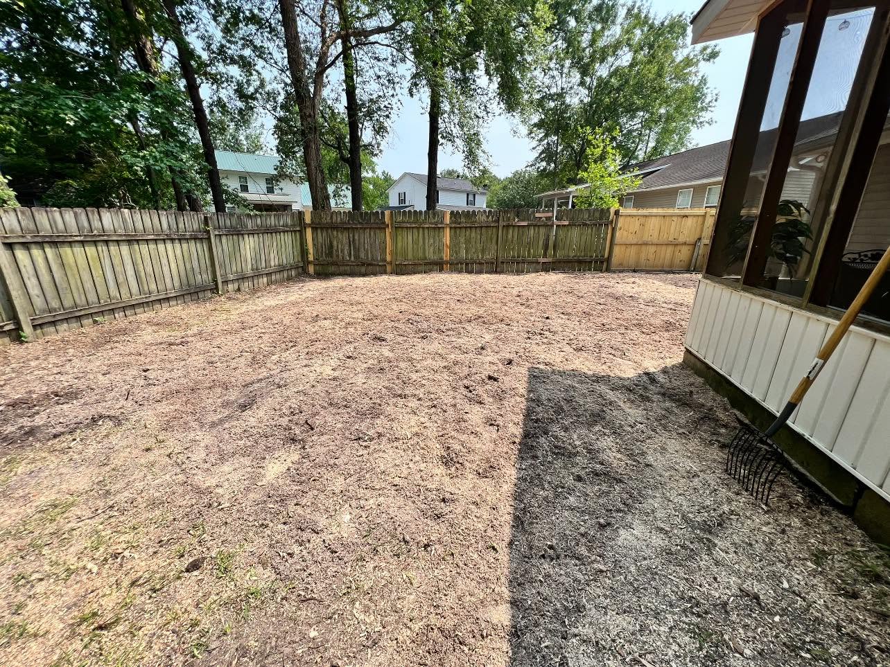 Fully cleared and leveled fenced residential backyard covered in fresh wood chip mulch after complete tree and stump removal, ready for new sod