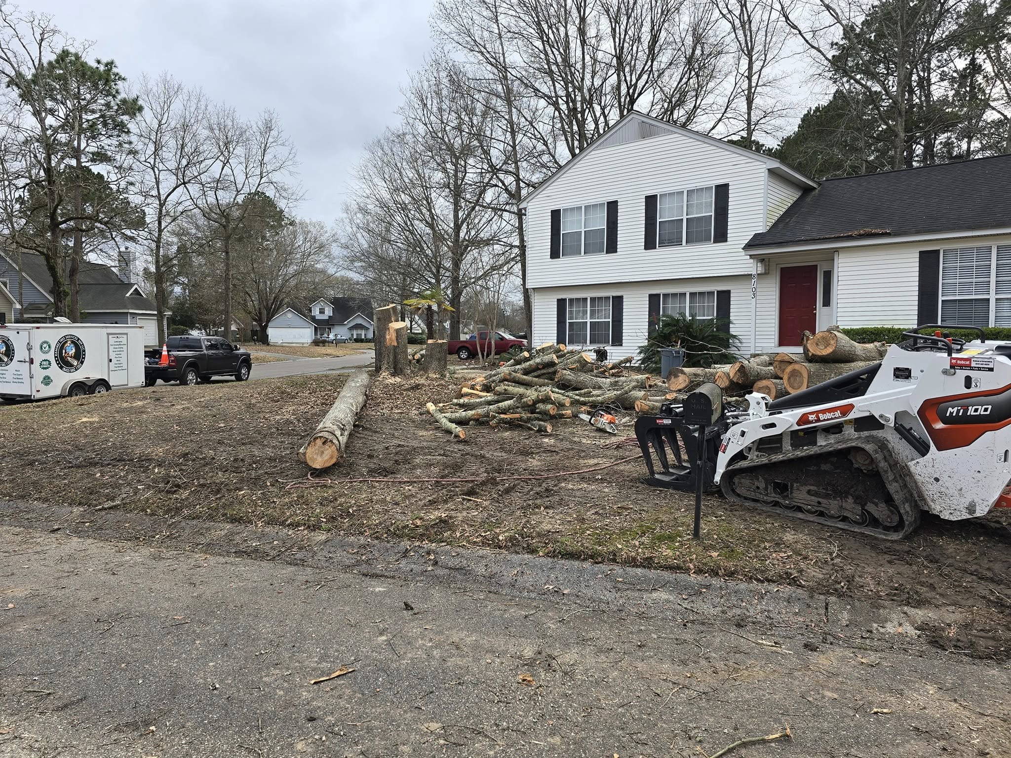 Bobcat MT100 and Ramirez Tree Services truck on site with large cut logs spread across a residential front yard after a full tree removal